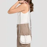 Cartera tipo bandolera Guess modelo Carrie, color beige, con solapa frontal y cierre magnético. Presenta el logo metálico de la marca en la parte central y detalles en cadena dorada. Incluye correa ajustable y extraíble.