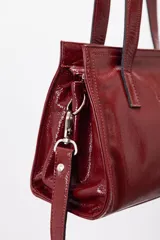 Cartera mini tote de cuero vacuno color bordó, con acabado charol, doble asa de mano y estructura rígida.
