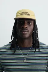 Gorra de 5 paneles de color amarillo claro con tejido ripstop, visera plana marrón de efecto desgastado y bordado frontal en negro. Cuenta con ajuste en la parte posterior.