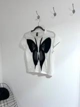 Remera corta negra de algodón con estampado de mariposa blanca.