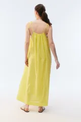 Vestido maxi solero amplio y largo de color amarillo, con escote redondo, frunces que otorgan vuelo, breteles finos ajustables con nudo en los hombros y bolsillos laterales.