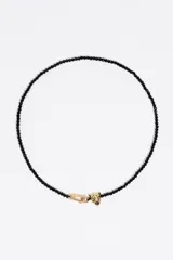 Collar de cuentas negras facetadas con un dije central en forma de cabeza de pantera dorada con detalles de cristales. Cuenta con un cierre de mosquetón metálico.