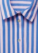 Camisa celeste con rayas verticales blancas, de corte recto, cuello camisero y mangas cortas murciélago. Cierre frontal con dos botones.