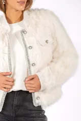 Chaqueta de piel sintética negra con corte recto, cuello redondo y cierre frontal con botones perlados. Presenta detalles de bordes con apliques de strass brillantes y bolsillos frontales con solapa.