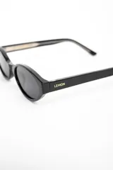Lentes de sol Lemon de armazón ovalado color negro y cristales oscuros, con detalle de la marca en letras doradas en la patilla.