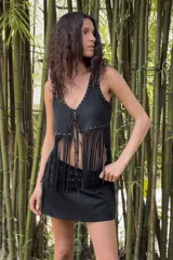 Chaleco negro de escote en pico y manga sisa, con detalle de tachas metálicas en el borde y cierre frontal con lazada. El bajo presenta un acabado con flecos largos.