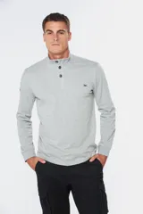 Remera de manga larga tipo buzo liviano, confeccionada en tejido jersey color gris melange. Presenta cuello mao con tapeta de tres botones y puños en rib.