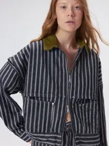 Campera de denim a rayas verticales con cuello de pana en color bordó. Presenta cierre frontal, mangas desmontables con cierre en los hombros, canesú en el pecho y bolsillos de parche cuadrados.