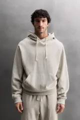 Sudadera con capucha color gris claro, de corte holgado, con bolsillo tipo canguro y cordones ajustables.