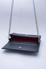 Cartera negra con textura símil cocodrilo y cadena metálica plateada.