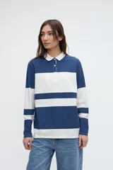 Remera polo de manga larga de algodón lavado, con diseño de rayas horizontales anchas en azul y blanco, cuello y cartera de botones en color blanco, y pequeños tajos laterales.