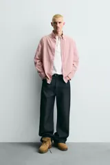 Camisa de corte relajado confeccionada en tejido de algodón, con diseño de rayas verticales en tonos rosados y blancos. Presenta cuello abotonado, cierre frontal de botones, manga larga con puños abotonados y bajo asimétrico.