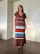 Vestido largo de tejido de punto de algodón, con diseño rayado en tonos marrón, celeste, blanco y rojo. Presenta escote en V con detalle de costura en contraste, mangas cortas, silueta holgada y aberturas laterales en el dobladillo.