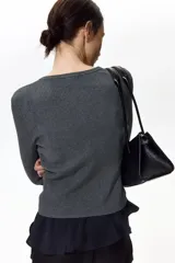 Saco corto de punto acanalado gris oscuro, con cuello redondo, manga larga y cierre frontal abotonado con detalles festoneados.