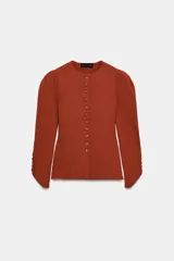 Chaqueta de punto color óxido, con cuello redondo, manga larga abullonada y cierre frontal con botones.