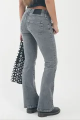 Pantalón de jean gris oscuro con efecto lavado, corte tiro bajo y diseño acampanado con bolsillos frontales decorativos.