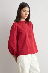 Blusa blanca de corte holgado con cuello mao y escote en V. Presenta detalles de bordado calado en el pecho y en los puños de las mangas tres cuartos.