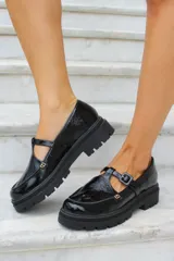 Zapato tipo guillermina en cuero charol color bordó, con suela track negra de goma, cierre con hebilla ajustable y detalle de herrajes metálicos dorados.