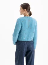 Cardigan de tejido de punto suave en color azul, con cuello redondo, cierre frontal y manga larga. Presenta pequeños apliques metálicos en forma de corazón distribuidos por toda la prenda.