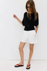 Top de punto color beige con cuello barco y mangas cortas anchas tipo murciélago. Cuenta con cintura entallada con ribete elástico y un cinturón fino de cuero sintético marrón con hebilla metálica dorada.