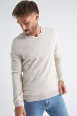 Sweater de tejido de punto color beige, con escote en V, mangas largas y puños y dobladillo acanalados. Presenta un pequeño logo bordado en el pecho.