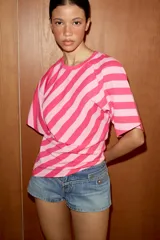 Top de algodón con estampado de rayas diagonales en tonos fucsia y rosado. Presenta cuello redondo, mangas cortas tipo murciélago y un diseño de bajo asimétrico.