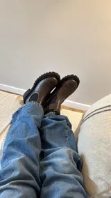 Bota tipo Chelsea de cuero marrón con suela track negra de goma. Presenta paneles elásticos laterales y una costura reforzada en la puntera. Incluye una correa de cuero desmontable con hebilla metálica.