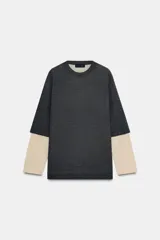 Jersey de cuello redondo y manga larga con diseño de doble capa, combinando un cuerpo en tono gris oscuro con mangas en tono beige.