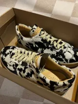 Zapatillas bajas con estampado animal print de vaca en blanco y negro, con cordones marrones y suela color caramelo.