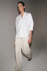 Camisa de algodón con cuello redondo y escote en pico, mangas tres cuartos con puños y bajo asimétrico redondeado.