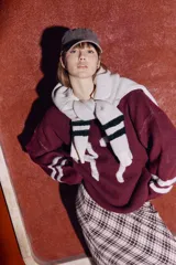 Sweater de punto color bordó con diseño de tipografía en relieve y rayas blancas en las mangas. Presenta un calce relajado y tejido suave.