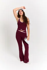 Conjunto deportivo compuesto por un top y un pantalón largo en color bordó. El top presenta un diseño con cuello redondo y ribetes blancos, con el logo 'bk.' estampado en el frente. El pantalón es de corte ajustado con cintura cruzada en V y detalle de ribete blanco, con terminación acampanada en los tobillos.