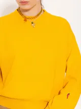 Sweater color marrón claro de tejido cerrado, con cuello redondo, mangas largas y largo a la primera cadera. Tiene un pequeño bordado rojo en el puño de la manga derecha.