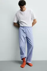 Set de pijama para hombre compuesto por una remera blanca de cuello redondo y mangas cortas, y un pantalón celeste a rayas verticales con cintura elástica y bolsillos laterales.