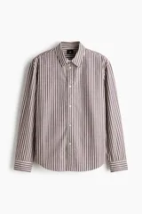 Camisa de algodón suave con cuello inglés, tapeta clásica y canesú en la espalda. Modelo de manga larga con puños abotonados y bajo levemente redondeado. Presenta diseño a rayas en tonos marrón y blanco.