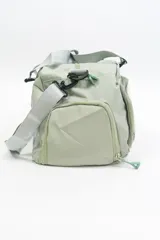 Bolso deportivo color rosa con detalles en beige y gris. Tiene doble asa de mano y correa de hombro ajustable. Cuenta con dos bolsillos frontales con cierre y logo de la marca en la esquina inferior derecha.