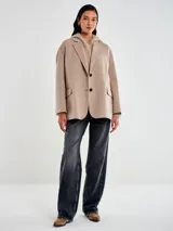 Chaqueta de paño color beige, de corte amplio y estructura clásica. Presenta solapas, cierre frontal con dos botones y bolsillos laterales con solapa.