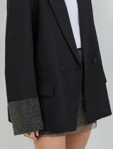 Blazer oversize negro con solapas de muesca, cierre de doble botón frontal y puños decorados con rhinestones plateados.