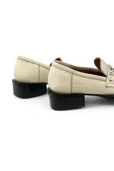 Mocasín color marfil de cuero, con detalle de tachas plateadas en la parte delantera y suela de goma negra.