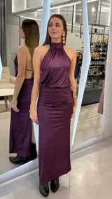 Vestido largo color lila con acabado brillante, escote halter y diseño drapeado en la zona de la cintura.
