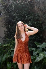 Vestido corto negro con escote en V profundo, estilo halter con tiras para atar al cuello. Presenta un diseño ajustado en el busto con tiras ajustables bajo el mismo que se cruzan y anudan en la espalda, y falda con volado en el ruedo con detalle de encaje.