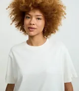 Remera de corte boxy con cuello redondo y mangas cortas. Confeccionada en algodón, presenta un diseño minimalista sin estampas con sisa caída.