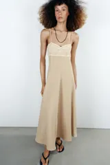 Vestido midi de color beige con escote recto adornado con un panel de encaje semitransparente, tirantes finos ajustables y falda fluida con cierre lateral con cremallera oculta.