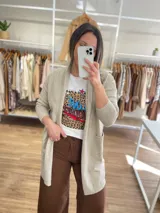 Saco largo color crema, de tejido de punto, con bolsillos laterales y corte recto.