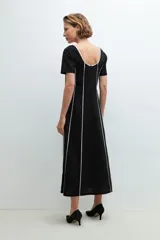 Vestido midi negro con rayas verticales blancas, escote redondo y cinturón negro con hebilla circular.