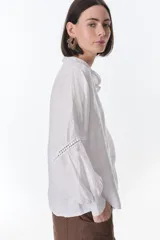 Camisa celeste de lino con botones, mangas largas abullonadas y detalles de crochet en el frente y los puños.