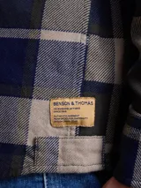 Camisa de manga larga en color azul noche con un patrón de cuadros finos en tonos rojos y verdes. Presenta cuello clásico, cierre frontal con botones y un bolsillo en el pecho con solapa.