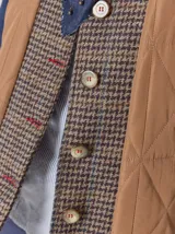 Campera de diseño híbrido con frente acolchado en color tostado, solapas y cuello en tejido de lana con patrón de cuadros tipo príncipe de gales, y mangas en paño de lana color azul marino. Cuenta con cierre frontal de botones.