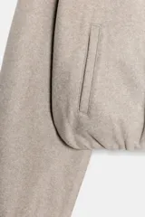 Cazadora de textura suave en color beige, con capucha, cierre frontal con cremallera, bolsillos laterales y bajo con acabado elástico.