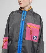 Campera larga color gris con cierre frontal azul, cuello alto y bolsillos laterales. Tiene un parche con diseño geométrico en el pecho. Marca Blue Steel.